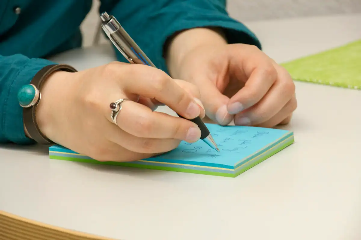 ペンを持ち、メモ帳に書き込んでいる手元